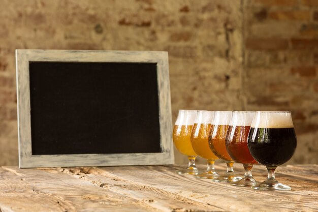 Gläser verschiedener Arten von dunklem und hellem Bier auf Holztisch in Linie und Tafel