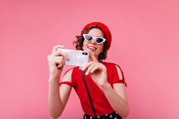 Glamouröse französische Dame in den Weinlesegläsern, die Foto von sich selbst machen. lockige Frau in der roten Baskenmütze, die selfie macht.