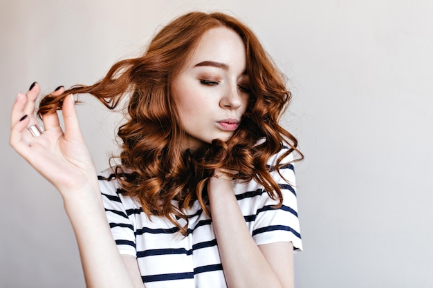 Glamouröse Ingwerfrau mit stilvollem Make-up, das aufwirft. Innenfoto des rothaarigen weiblichen Modells im gestreiften T-Shirt, das Fotoshooting genießt.