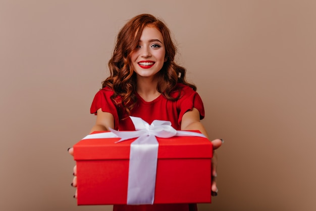 Glamouröse junge frau, die weihnachtsgeschenk hält. wunderbares lockiges weibliches modell, das sich auf neujahrsparty vorbereitet.