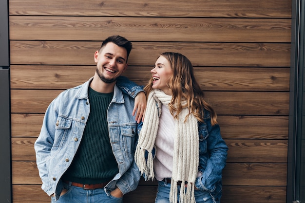 Glamouröses Mädchen im weißen Schal, das Freund mit Liebe betrachtet. Innenporträt des schönen europäischen Mannes, der Freizeit mit niedlicher Freundin verbringt.