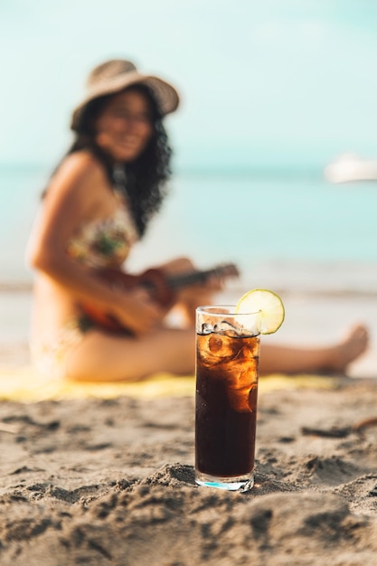 Glas Cola mit Eis und Frau am Sandstrand