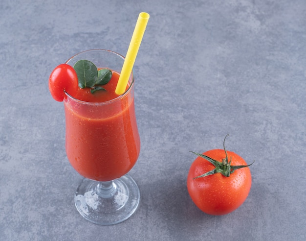 Glas frischen Tomatensaft und Tomate auf grauem Hintergrund.