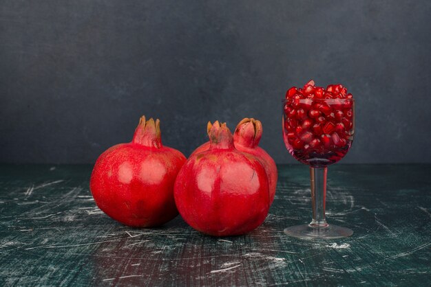 Kostenloses Foto glas granatapfelkerne und granatapfel auf marmoroberfläche.