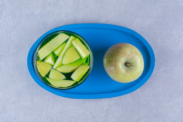 Glas Kiwisaft und Apfel auf einer Holzplatte auf Marmortisch.