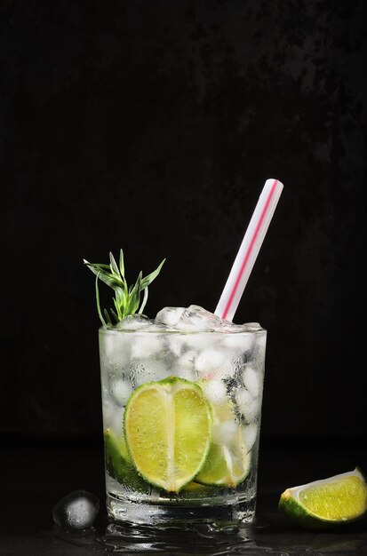 Glas Limonade auf dunklem Hintergrund. Vertikaler Rahmen, selektiver Fokus. Hausgemachtes Getränk mit Limette, Estragon, Mineralwasser und Eiswürfeln. Kalte frische Limonade Idee