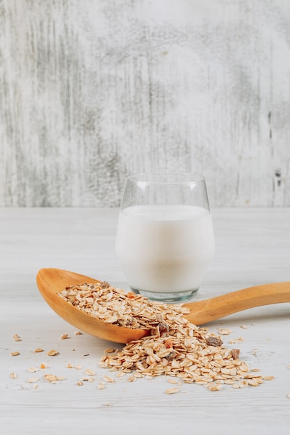 Glas Milch mit Hafer in der Holzlöffel-Seitenansicht auf einem weißen hölzernen Hintergrund