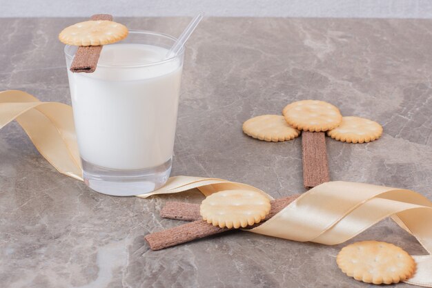 Glas Milch mit Keksen und Band auf Marmortisch.