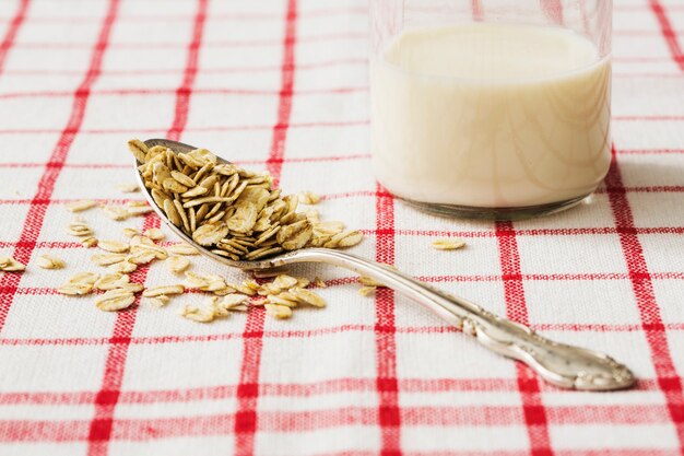 Glas Milch mit trockenen Hafern blättert auf dem alten Löffel ab