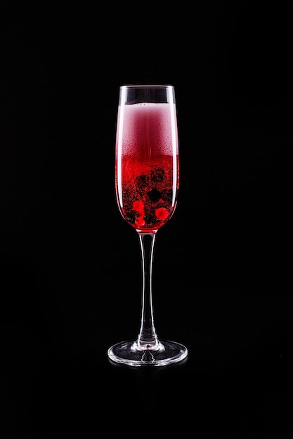 Glas mit Beeren und rotem Champagneralkoholcocktail steht auf schwarzem Hintergrund