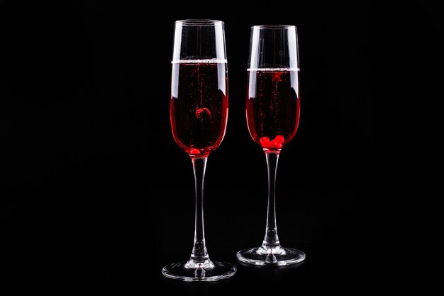 Glas mit Beeren und rotem Champagneralkoholcocktail steht auf schwarzem Hintergrund