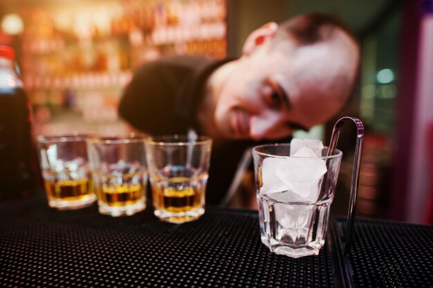 Glas mit Eis und Zangen mit drei Whiskygläsern Hintergrund lustiger Barkeeper