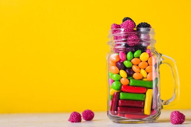 Glas mit Süßigkeiten auf hellem gelbem Hintergrund