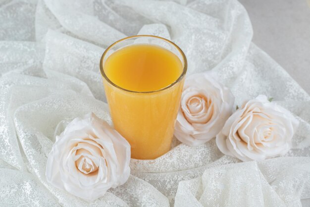 Glas Orangensaft mit Blumen auf weißem Stoff