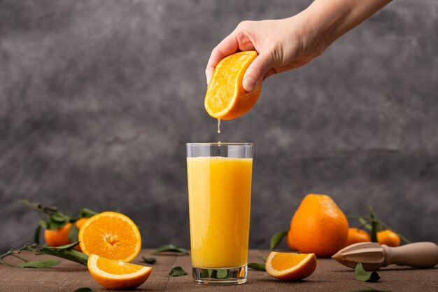 Glas Orangensaft und eine Person, die eine Orange darin drückt