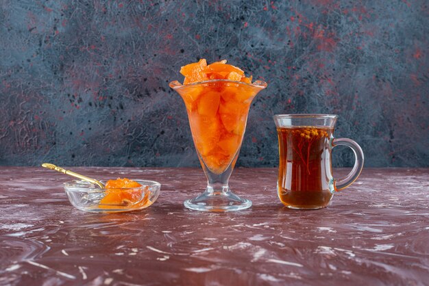 Glas Quittenmarmelade und Glas Schwarztee auf dem Tisch.