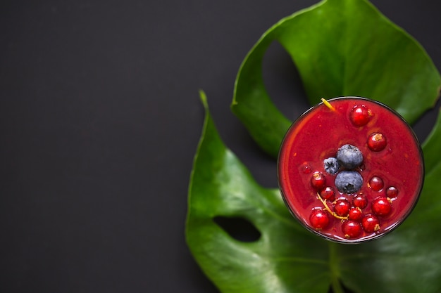 Kostenloses Foto glas smoothie mit beeren auf monstera-blatt über dem schwarzen hintergrund