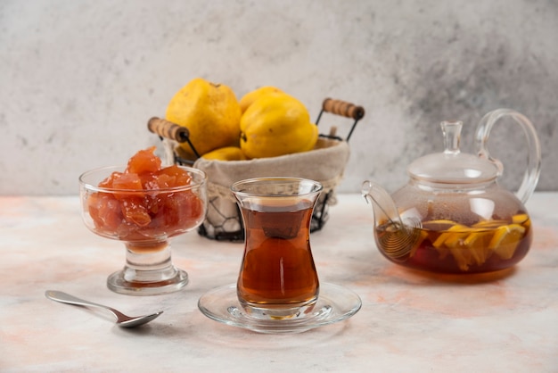 Glas Tee, Marmelade und Quittenfrüchte auf Holzplatte.