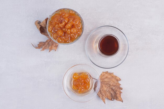 Glas Tee und Beerenmarmelade auf weißem Tisch.