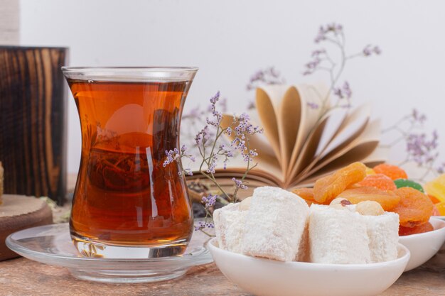 Glas Tee, verschiedene Süßigkeiten und getrocknete Aprikosen auf Marmortisch.