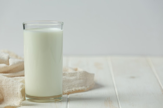Glas und Flasche Milch auf weißer Holzoberfläche