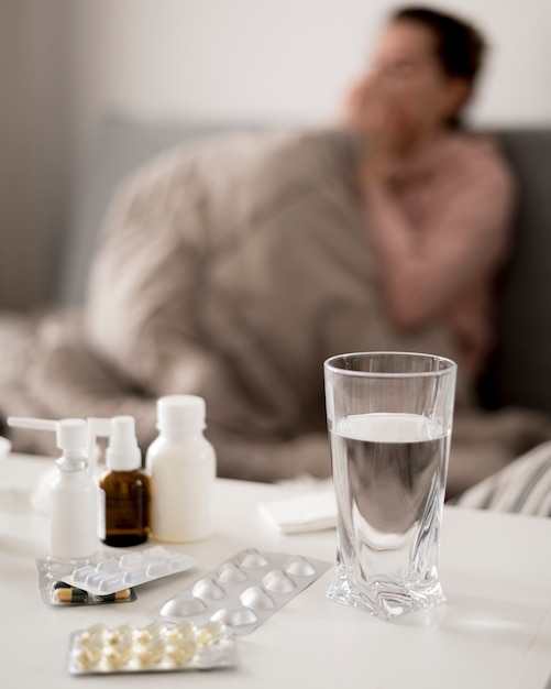 Glas Wasser und Pillen mit verschwommener kranker Person
