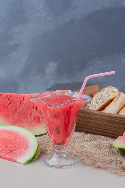 Glas Wassermelonen-Smoothie und Brotkorb auf weißem Tisch.