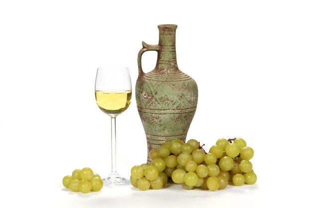 Glas Weißwein neben einem Weinkrug mit grünen Trauben auf einem Weißwein