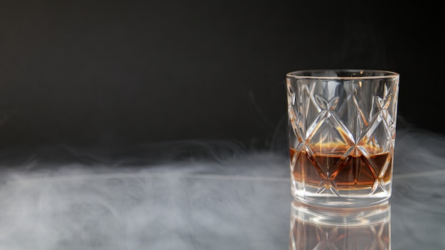 Glas Whisky auf einem Tisch, umgeben von Rauch vor einem schwarzen Hintergrund