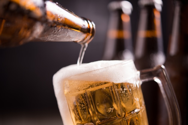 Glasflaschen Bier mit Glas und Eis auf dunklem Hintergrund