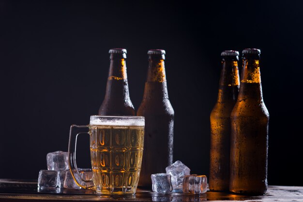 Glasflaschen Bier mit Glas und Eis auf dunklem Hintergrund