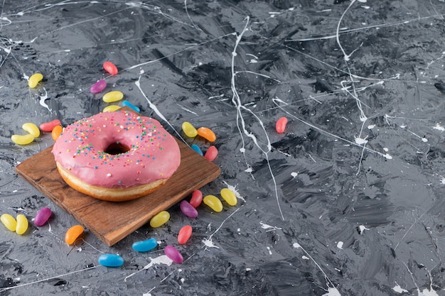 Glasierter Donut auf einem Brett neben bunten Süßigkeiten auf dem gemischten Tisch.