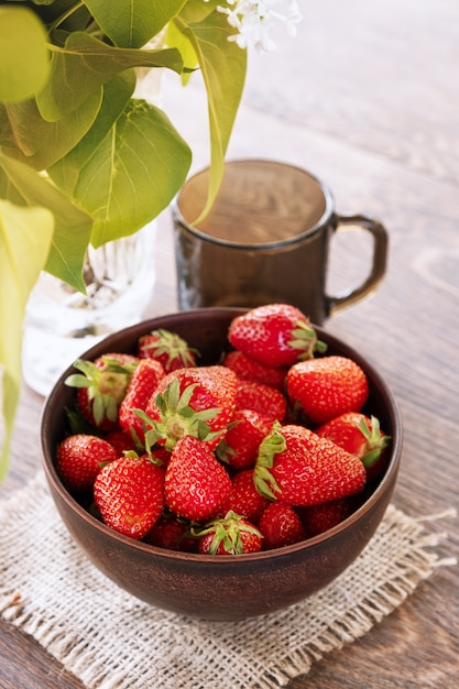 Glaskeramikschale mit reifen Fresserdbeeren und dunklem Glas auf einem Esstisch.