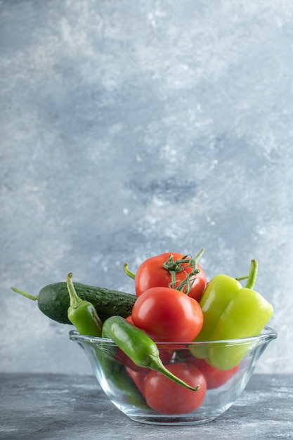 Glasschüssel mit frischem reifem Gemüse auf Marmorhintergrund