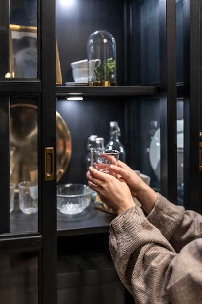 Glastasse in weiblichen Händen auf dem Hintergrund eines Sideboards mit schönen Vintage-Gerichten.