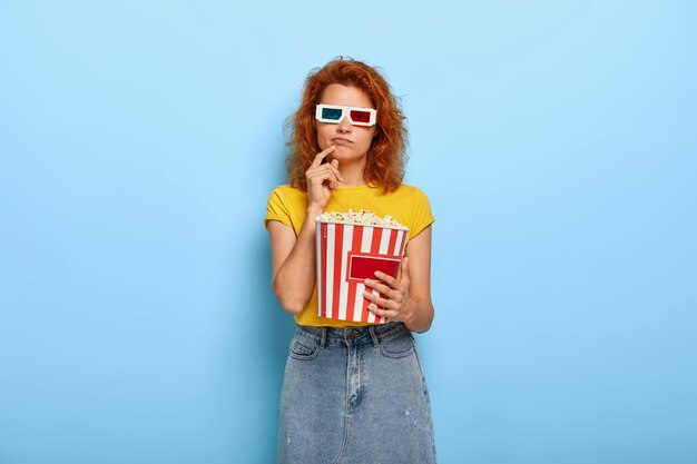 Gleichgültiges Ingwer charmantes Mädchen hält Eimer mit Popcorn