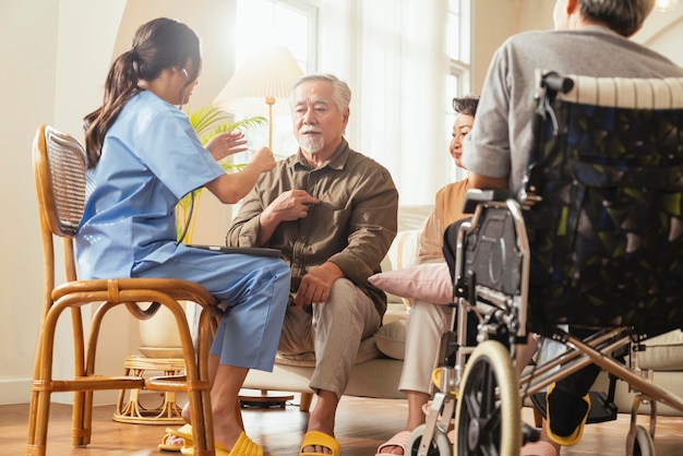 Glück Fröhliche ältere Frauen und Männer, die mit einer weiblichen Pflegekraft sprechen, die eine Gesundheitsprüfung im Wohnbereich durchführt, Hausmeister mit einem älteren Paar, das im Wohnzimmer eines Pflegeheims sitzt
