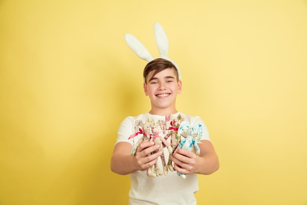 Glücklich. Dekorieren. Kaukasischer Junge als Osterhase auf gelbem Studiohintergrund. Fröhliche Ostergrüße. Schönes männliches Modell. Konzept der menschlichen Gefühle, Gesichtsausdruck, Feiertage. Copyspace.