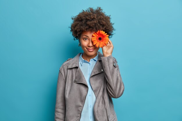 Glücklich erfreut junge Afroamerikanerin Floristin macht Strauß Gerbera Gänseblümchen, arbeitet im Blumenladen, trägt graue Jacke, hat angenehmes Lächeln,