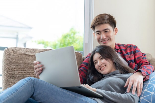 Glücklich junge hübsche Frau und gutaussehender Mann, die zu Hause Laptop-Computer auf dem Sofa im Schlafzimmer verwendet