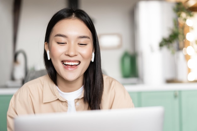 Glücklich lächelnde asiatische mädchen, die auf laptop-videokonferenz-studentin spricht, die online-webinar unter d...