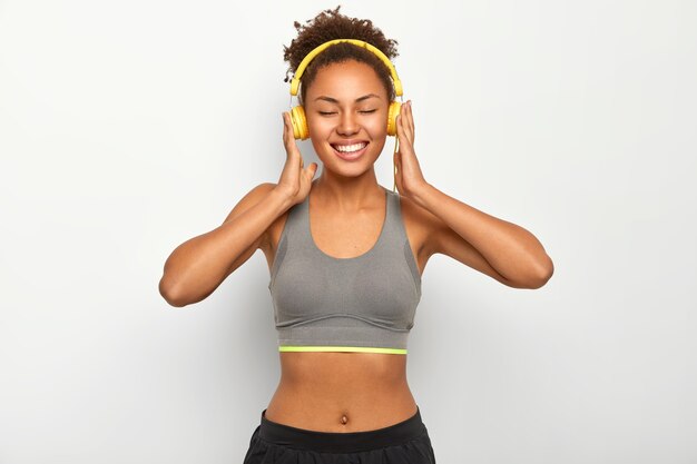 Glücklich lächelnde Frau entspannt sich nach Übungen, trägt sportliche Kleidung, hört Musik über moderne Kopfhörer, hat gute Laune