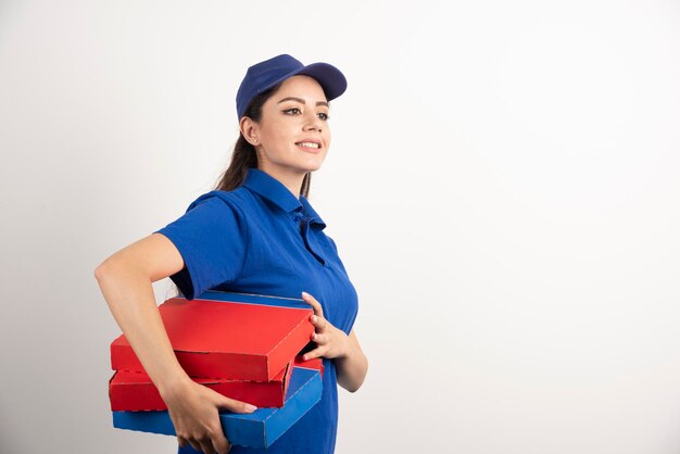Glücklich lächelnde Liefermädchen in blauer Uniform mit Pizzakartons zum Mitnehmen auf weißem Hintergrund. Foto in hoher Qualität