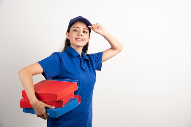 Glücklich lächelnde Liefermädchen in blauer Uniform mit Pizzakartons zum Mitnehmen auf weißem Hintergrund. Foto in hoher Qualität