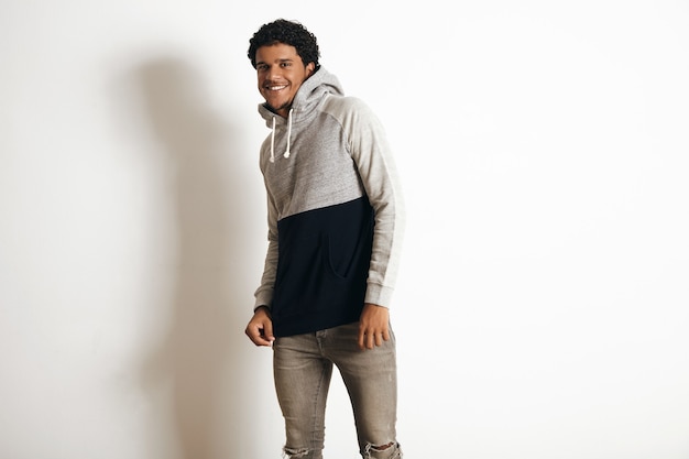 Glücklich lächelnder Latino-Typ trägt leeren grauen schwarzen Pullover mit Kapuze und notleidende Jeans, lokalisiert auf Weiß