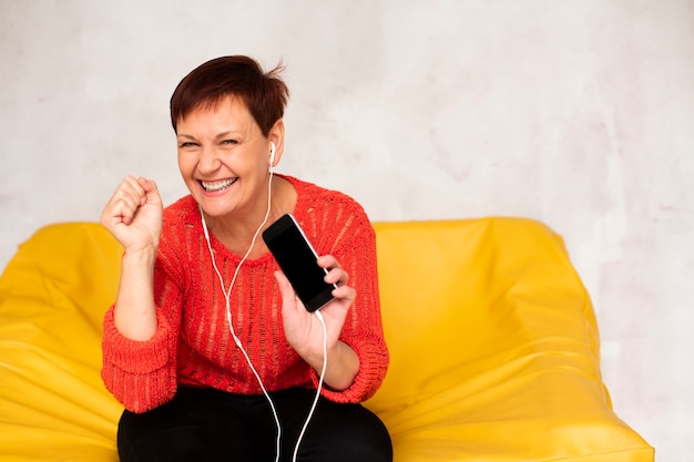 Glückliche ältere Frau auf hörender Musik der Couch