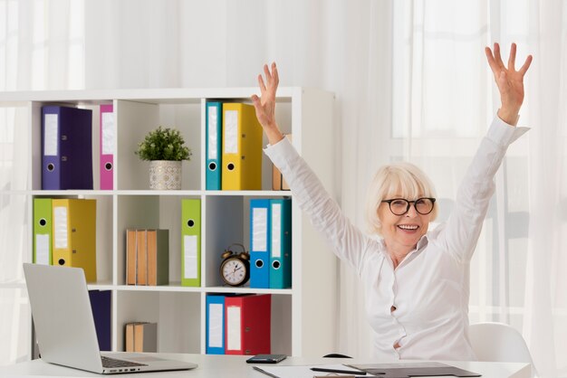 Glückliche ältere Frau, die auf ihrem Büro sitzt