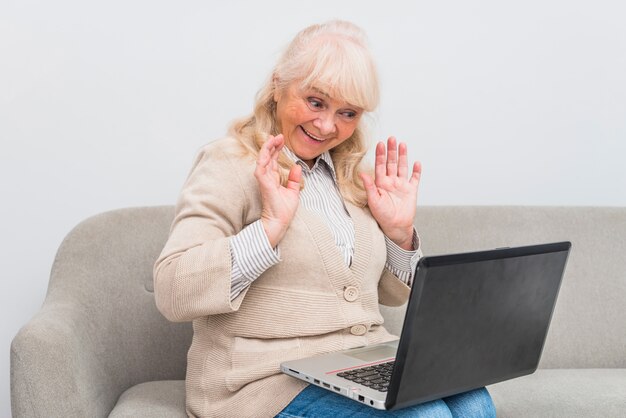 Glückliche ältere Frau, die Videochat auf wellenartig bewegender Hand des Laptops hat