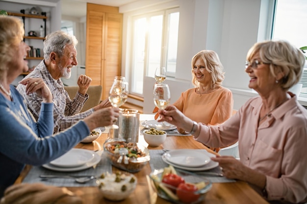 Glückliche ältere Freunde, die zusammen zu Mittag essen und mit Wein am Esstisch anstoßen