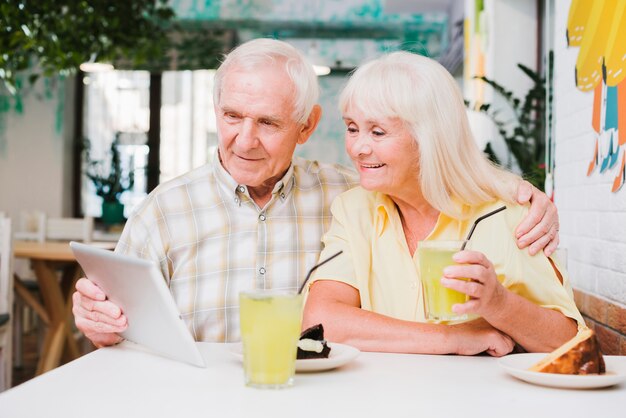 Glückliche ältere Paare im Café, das Auffrischungsgetränk genießt und Tablette verwendet